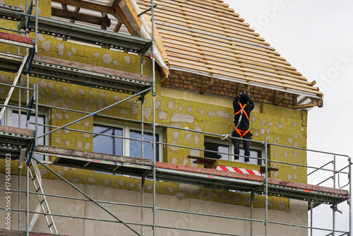 Worker on scaffolding insulating house facade with mineral wool during construction