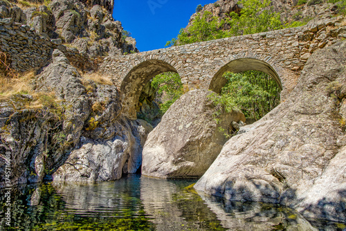 The old Ponte di l'Accia stone bridge on the Scala di Santa Regina hiking trail looks like a face near Corscia in central Corsica in the sunlight and beautiful water reflection