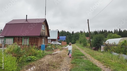 Slow motion. A child, a five-year-old girl, runs along a road on a summer day in a village.