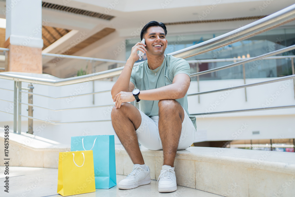 Obraz premium Smiling young man sitting in a mexican shopping mall making a phone call