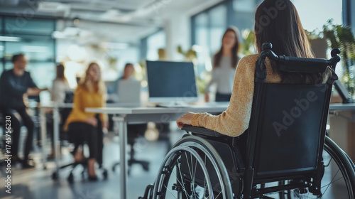 Close-up of wheelchair userâs hand pressing screen to upload a project, blurred team of colleagues smiling around shared workspace