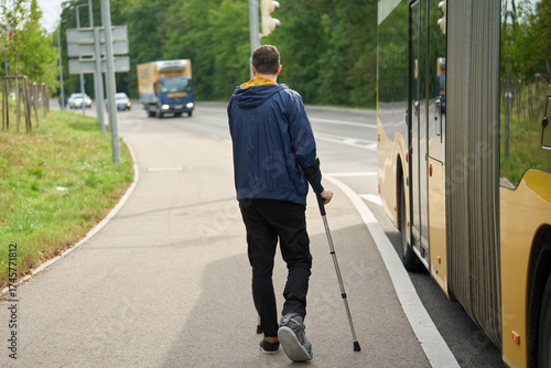 Person with injured leg walking with crutches near road Injured leg in boot, crutches, city sidewalk, bus, movement
