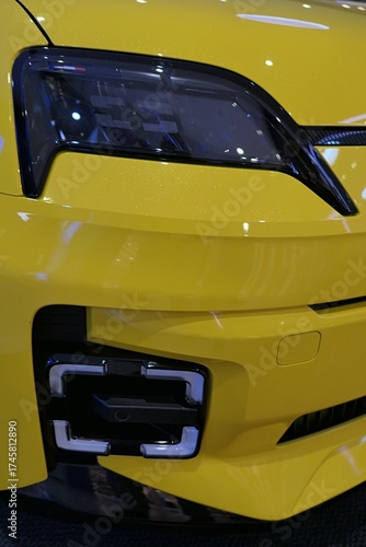 Headlight and stylish square shaped fog light on modern B-Segment french battery electric car, yellow chassis color. 