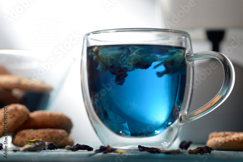 Blue butterfly pea tea in glass cup with cookies on blue wooden table