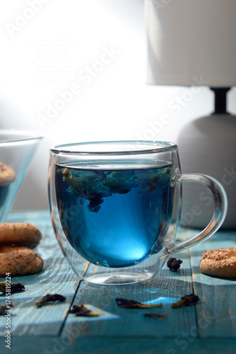 Blue butterfly pea tea in glass cup with cookies on blue wooden table