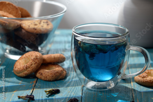 Blue butterfly pea tea in glass cup with cookies on blue wooden table