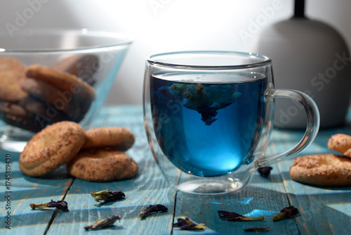 Blue butterfly pea tea in glass cup with cookies on blue wooden table