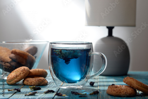 Blue butterfly pea tea in glass cup with cookies on blue wooden table