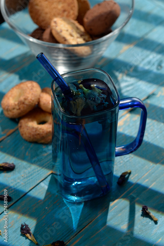 Blue butterfly pea tea in glass cup with cookies on blue wooden table