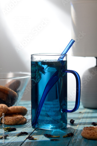 Blue butterfly pea tea in glass cup with cookies on blue wooden table