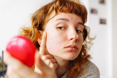 young woman looks at problematic facial skin in mirror