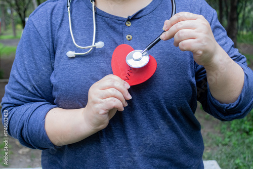 Obese Latina woman holding a broken heart and a stethoscope, heart problems concept