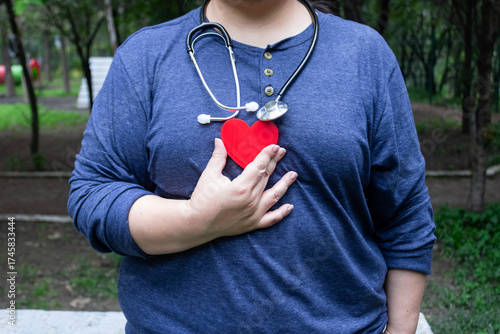 An obese woman holds a heart and a stethoscope because she is worried about her health.