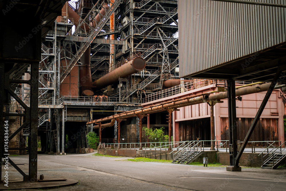 Naklejka premium Close-up of rusted metal pipelines and intricate steel walkways in an abandoned factory setting. Highlights industrial textures and architectural details.