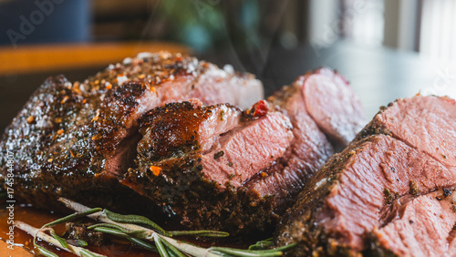 Freshly sliced, succulent roasted leg of lamb, releasing tempting steam. Served on a wooden board with aromatic rosemary and herbs, this juicy and perfectly cooked meat is the ultimate hearty meal.