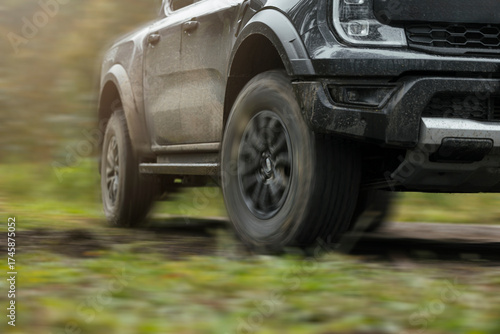 Off-road black pickup truck with mud tires driving on grassy trail outdoors with motion effect