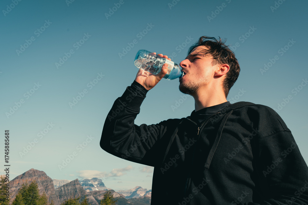 Fototapeta premium Man hydrates with bottled water outdoors with mountain view.