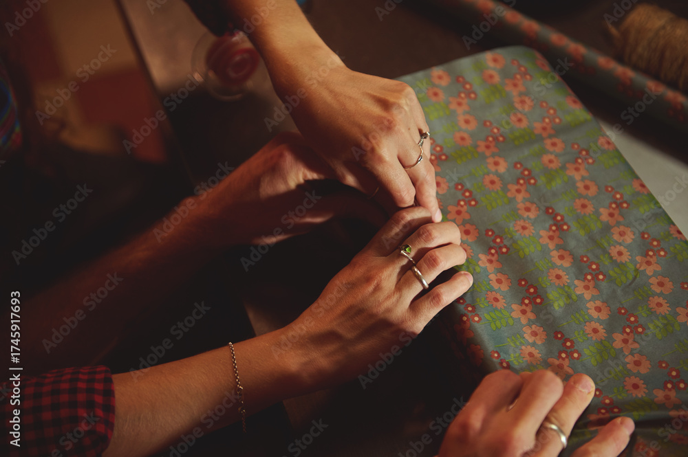 Obraz premium Pair Of Hands Sewing Fabric With Floral Pattern On Table, Crafting Moment Of Shared Sewing, Friendship And Creative Work