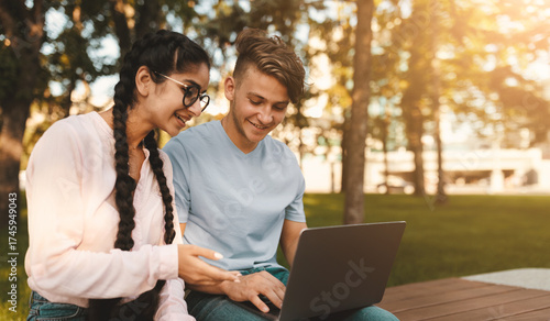 Friendly international college classmates preparing for lectures outdoors, sitting in park or college campus with laptop. Break between classes concept