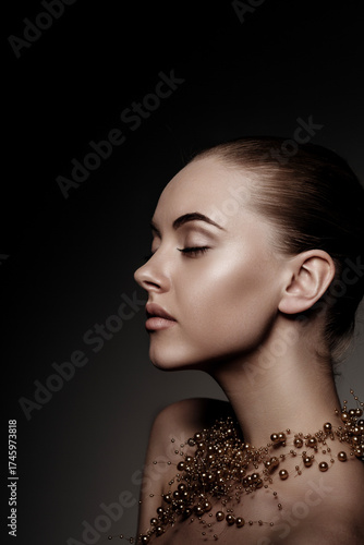 Artistic side profile portrait of a woman with smooth skin and elegant gold pearl necklace. Minimalistic beauty, soft lighting, dark background, luxury and sophistication concept.