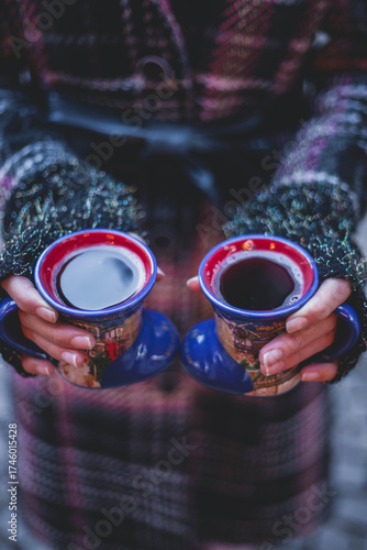 Vertical close up on woman's hans holding two cup of mulled red wine. Females hands holding hot drinks, while wearing fingerless gloves and winter coat. Christmas market concept