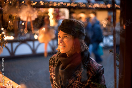 Beautiful woman is with interest looking at small ballerina figure as Christmas decoration on traditional Christmas market in Germany. Portrait of cheerful model in winter outfit fascinated Christmas 