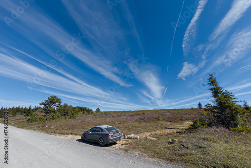 Car parked on gravel road under wide blue sky with streaked clouds and open highland landscape in Dolly Sods, West Virginia