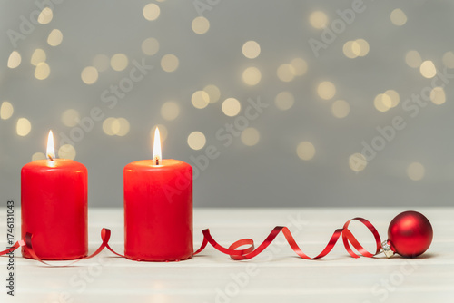 Two red burning candles and a ribbon with a red spruce tree baubles on a blurred background with bokeh. Christmas background, greeting card.