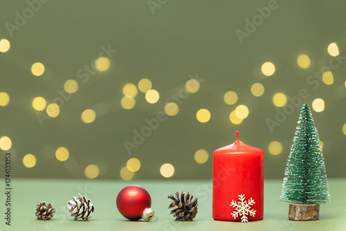 Red candle, red Christmas tree ball, pine cones, and spruce on a green background with bokeh. Christmas background, card.