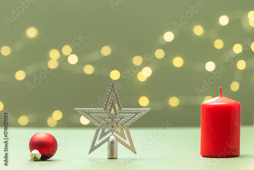 Red candle, Christmas tree star and red Christmas tree ball on a green background with bokeh.