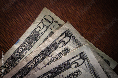 Old American paper currency including $5 and $20 bills fanned out on a dark wooden surface. Concept of US finance, business wealth, inflation, or economy.