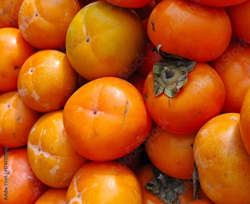 selective image of fresh ripe persimmon fruit (Diospyros kaki) displayed together at a local market for sale. ideal for fruit background and vegetarian diet or natural food design theme