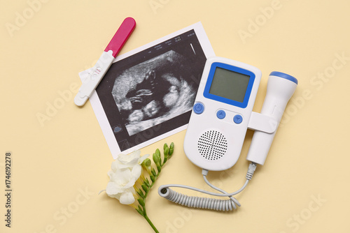 Fetal doppler with sonogram image, pregnancy test and flower on yellow backgr...