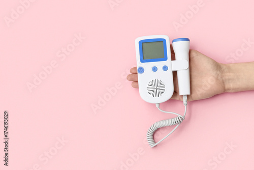 Fototapeta Female hand with fetal doppler on pink background