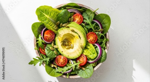 Fresh avocado salad with spinach tomatoes red onion and pumpkin seeds in a wooden bowl on a white surface creates a healthy and vibrant meal option for lunch or dinner.