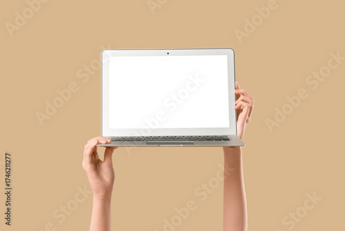 фотографія Female hands holding modern laptop with blank screen on beige background