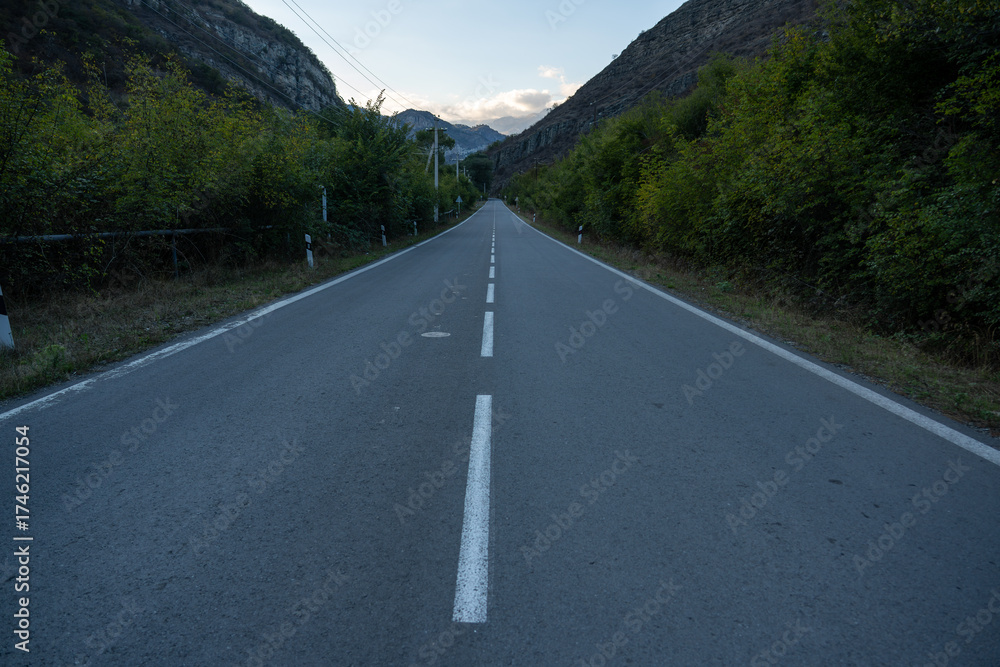 Fototapeta premium Straight empty highway between forest hills with dramatic sky
