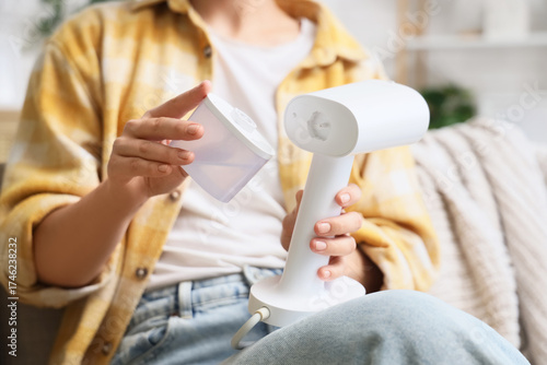 Fényképezés Young woman attaching water tank to modern garment steamer at home, closeup