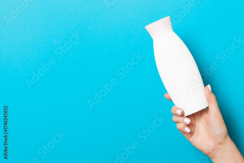 Female hand holding cream bottle of lotion isolated. Girl give tube cosmetic products on blue background