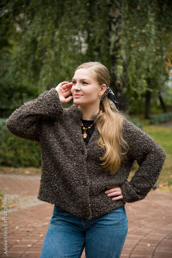 Naklejka premium young beautiful blonde woman with long hair in blue jeans and brown handmade sweater posing in autumn park
