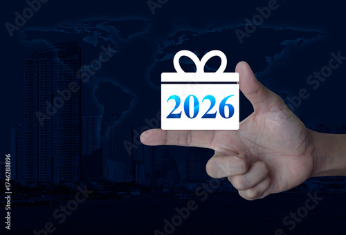 Fototapeta Naklejka Na Ścianę i Meble -  Gift box happy new year 2026 flat icon on finger over world map, modern city tower and skyscraper, Business shopping online concept, Elements of this image furnished by NASA