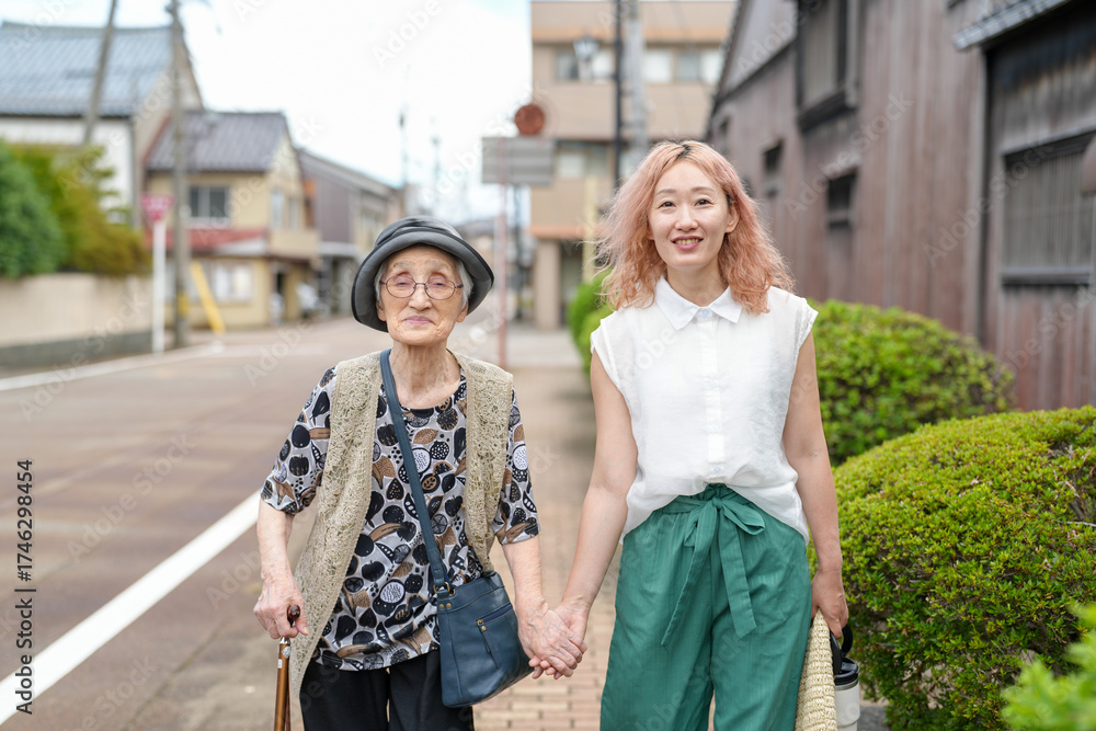 Naklejka premium Two women walking down a street, one of them is wearing a hat. The woman in the hat is holding the hand of the woman in the white shirt