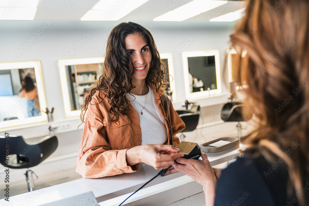 © Koldo_Studio - Happy woman smiling, completing a contactless payment using a credit card and pos terminal at a hairdressing salon