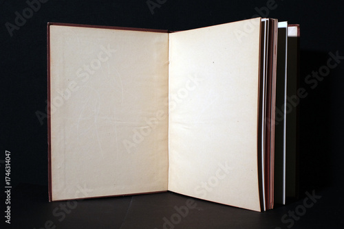 Old book open to a blank beige page, photographed against a black background. The image conveys the material beauty of timeworn paper and classic bookbinding craftsmanship.
