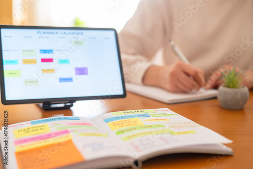 Person organizing daily tasks and appointments for work and home responsibilities using a physical planner and a digital calendar on a tablet for an organized lifestyle