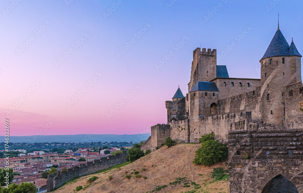 Obraz premium Medieval fortress walls and towers of Carcassonne at sunset, France. Old medieval walls of Carcassonne illuminated by purple sunset sky.