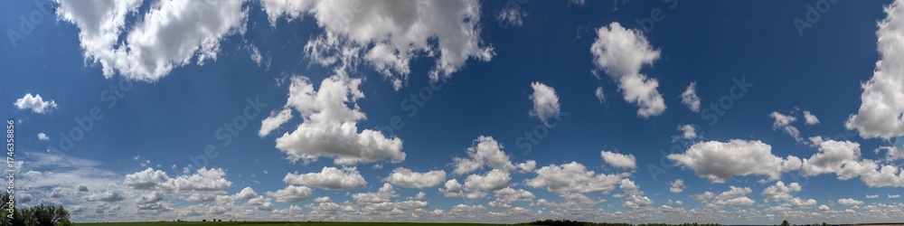 Obraz premium Vast blue sky filled with fluffy white clouds over a green landscape during midday in tranquil countryside