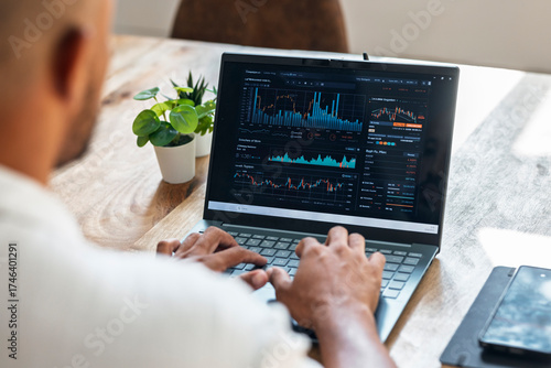 Trader analyzing financial data on laptop at home office workspace