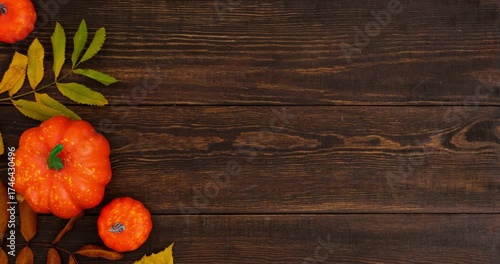 Autumn composition with pumpkins and fallen colorful leaves on brown wooden background with place for text. 4K looped stop motion animation