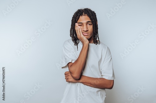 Young person with braided hair in a white shirt looking bored.